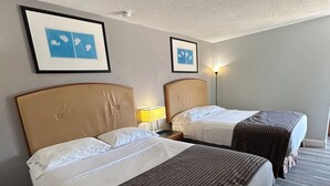 A hotel room with two beds, each with a headboard and a bedside lamp. There are framed pictures on the wall above the beds. - Travel Inn & Suites (Emporia)