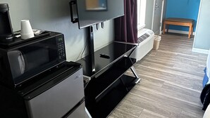A compact hotel room with a flat-screen TV, a mini-fridge, a microwave, and a small table. - Travel Inn & Suites (Emporia)