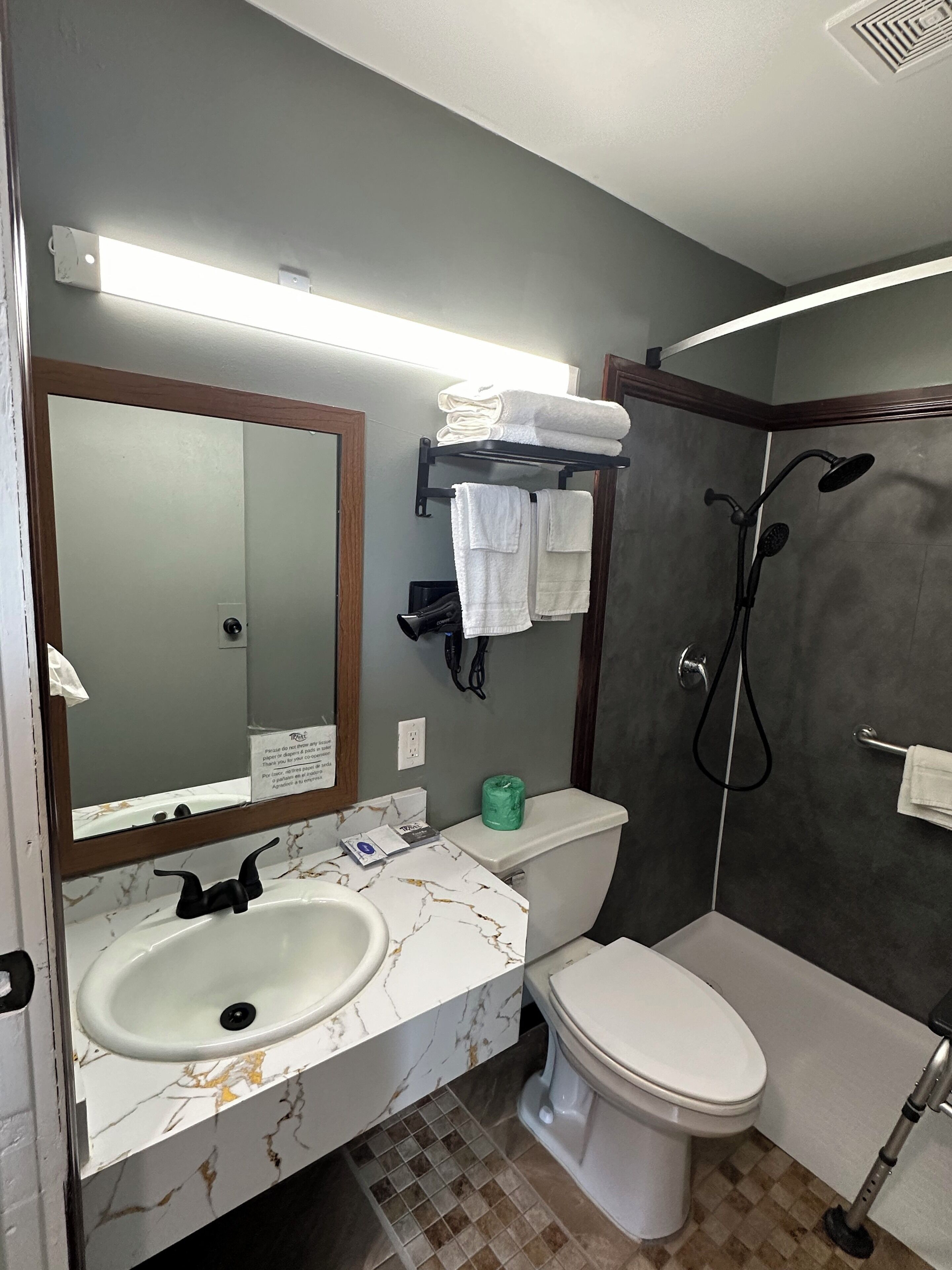 Un baño con lavamanos de mármol, inodoro, ducha y barra para toallas.