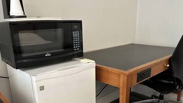 Een kleine kitchenette met een witte minikoelkast, een zwarte magnetron en een koffiezetapparaat.