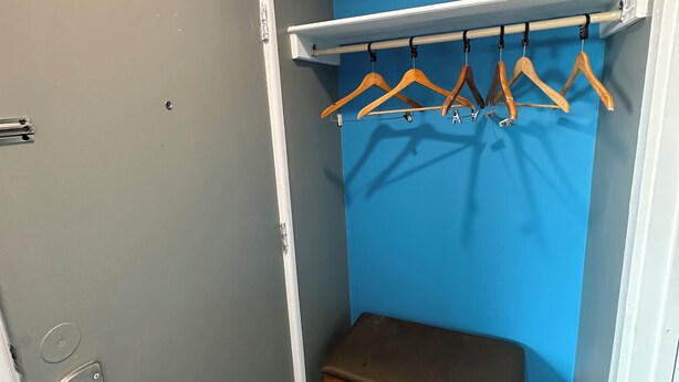 A small room with a bench, a coat rack with wooden hangers, and a blue wall. - Travel Inn & Suites (Emporia)