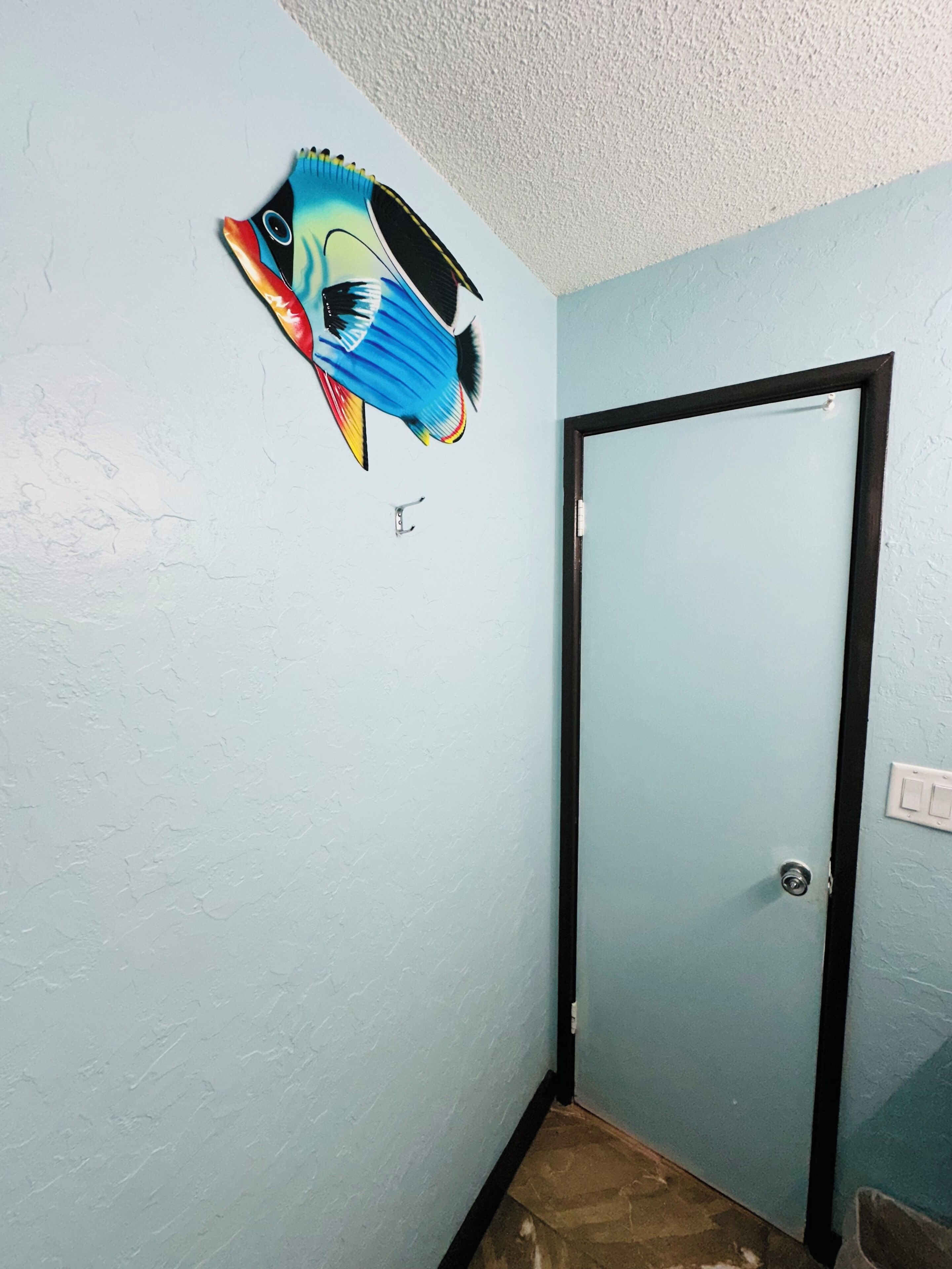 A room with light blue walls, a black-framed door, and a colorful fish mural on the wall.