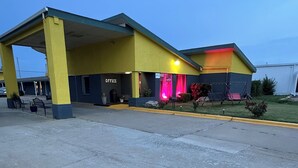 A yellow building with an 'Office' sign, a covered parking area, and a small garden with a swing set. - Travel Inn & Suites (Emporia)