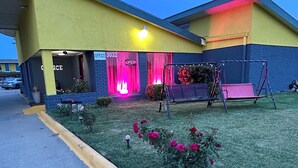 A building with a yellow and blue facade, a sign indicating an office, and a swing set in the yard. - Travel Inn & Suites (Emporia)