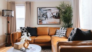 A living room with a brown leather sofa, a round coffee table, and a floor lamp. There is a painting on the wall and a plant in the corner. - Peachtree/Royal Oak`s Sweet Spot/King Bed (Royal Oak)