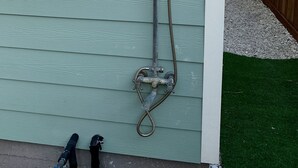 A metal outdoor showerhead mounted on a wall with a hose and a flexible connector.