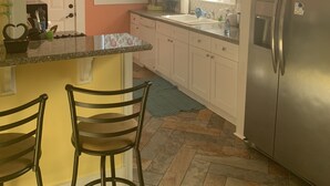 A kitchen with a central island, two bar stools, a stainless steel refrigerator, and a window with floral curtains.