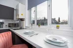 A modern kitchen with a large window, white countertops, and a pink chair.