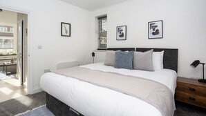 Een slaapkamer met een bed, nachtkastjes, een raam en ingelijste foto's aan de muur.