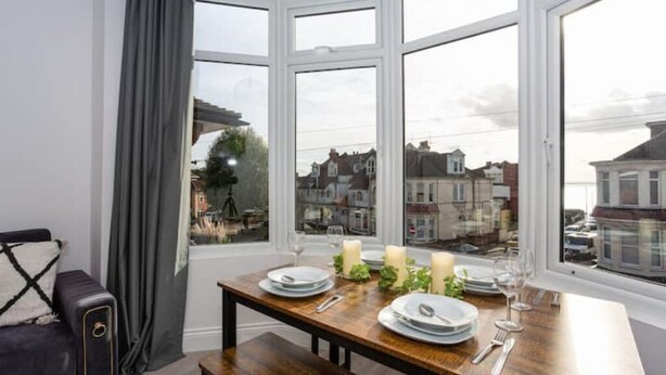 A dining area with a table set for four, large windows, and a view of buildings outside. - Trendy 2 Bed Flat, close to Beach & Restaurants (Southend-on-Sea)