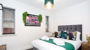 Ein ordentlich eingerichtetes Schlafzimmer mit einem Bett, Nachttischen und einem Neon-Leuchtschild an der Wand.