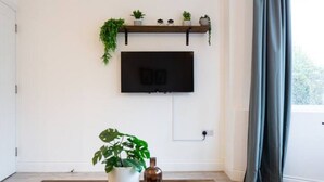 Ein Wohnzimmer mit einem an der Wand montierten Fernseher, einem Couchtisch, einer Topfpflanze und einer Fernbedienung.