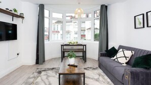 Ein modernes Wohnzimmer mit großem Fenster, einer Couch, einem Couchtisch und einem an der Wand befestigten Fernseher.