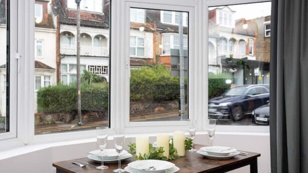Ein Esstisch mit Tellern, Gläsern und Kerzen, platziert neben einem Fenster mit Blick auf eine Wohnstraße.