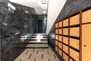 A modern hallway with marble walls, a wooden locker area, and a staircase leading to an elevator.