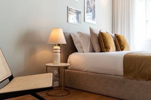 A neatly arranged hotel room with a bed, a bedside table with a lamp, a chair, and framed pictures on the wall.