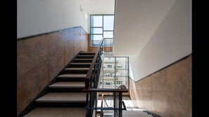 A modern staircase with marble walls and a metal railing, leading to a balcony with a view of buildings.