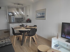 Un salon moderne avec une table de salle à manger ronde, des chaises noires, un canapé, un téléviseur et une bibliothèque.