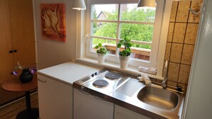 Een compacte keuken met een raam, een spoelbak, een fornuis en een klein tafeltje met een bloemenvaas.