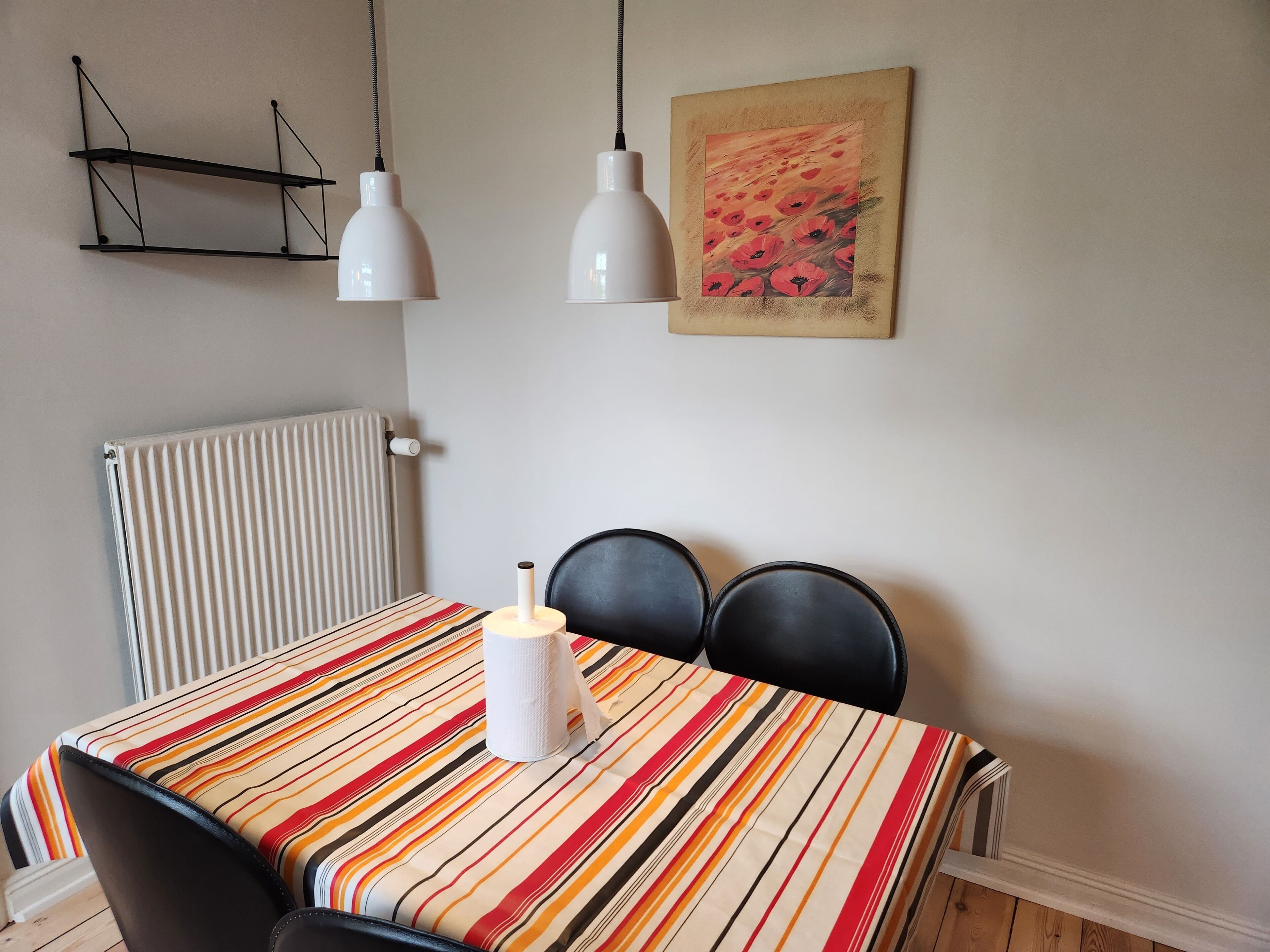 Ein Essbereich mit gestreifter Tischdecke, zwei Stühlen, einem weißen Heizkörper und zwei Pendelleuchten.