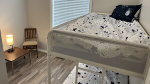 A child's bunk bed with a star-patterned mattress and pillow, a wooden chair, a small table with a lamp, and a window with blinds. - Home away from Home
Main Floor of Home (Three Hills)