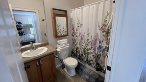 A bathroom with a sink, toilet, and shower curtain. - Home away from Home
Main Floor of Home (Three Hills)