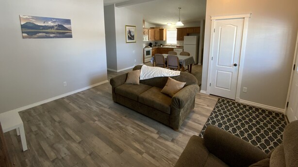 A living room with a brown sofa, a patterned rug, and a dining area with a table and chairs. - Home away from Home
Main Floor of Home (Three Hills)
