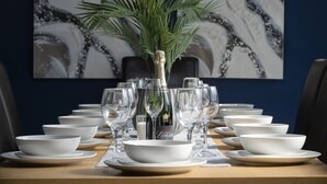 A dining table set with white bowls, plates, and wine glasses, with a bottle of champagne in the center. - Margate Beach house (Cliftonville)