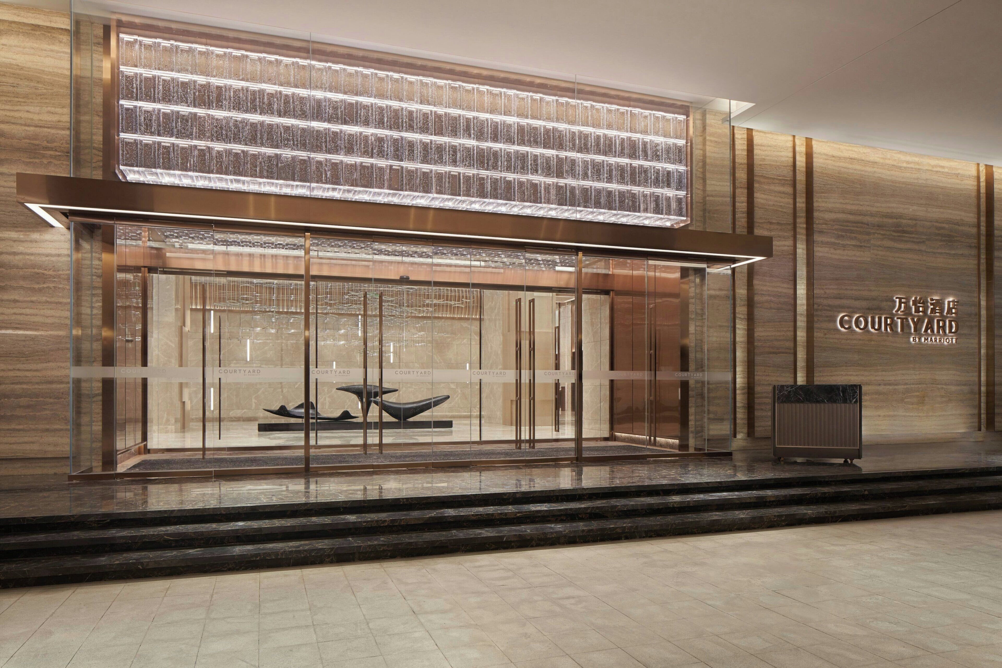 A modern hotel entrance with a glass facade, a large illuminated panel above the doors, and the name 'Courtyard' displayed on the wall.