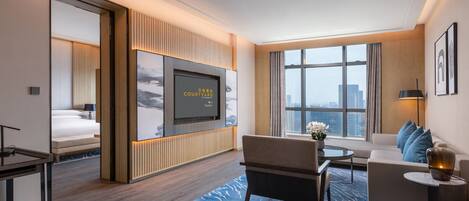Una habitación de hotel moderna con un televisor grande, un sofá, una mesa de comedor y vistas a la ciudad.