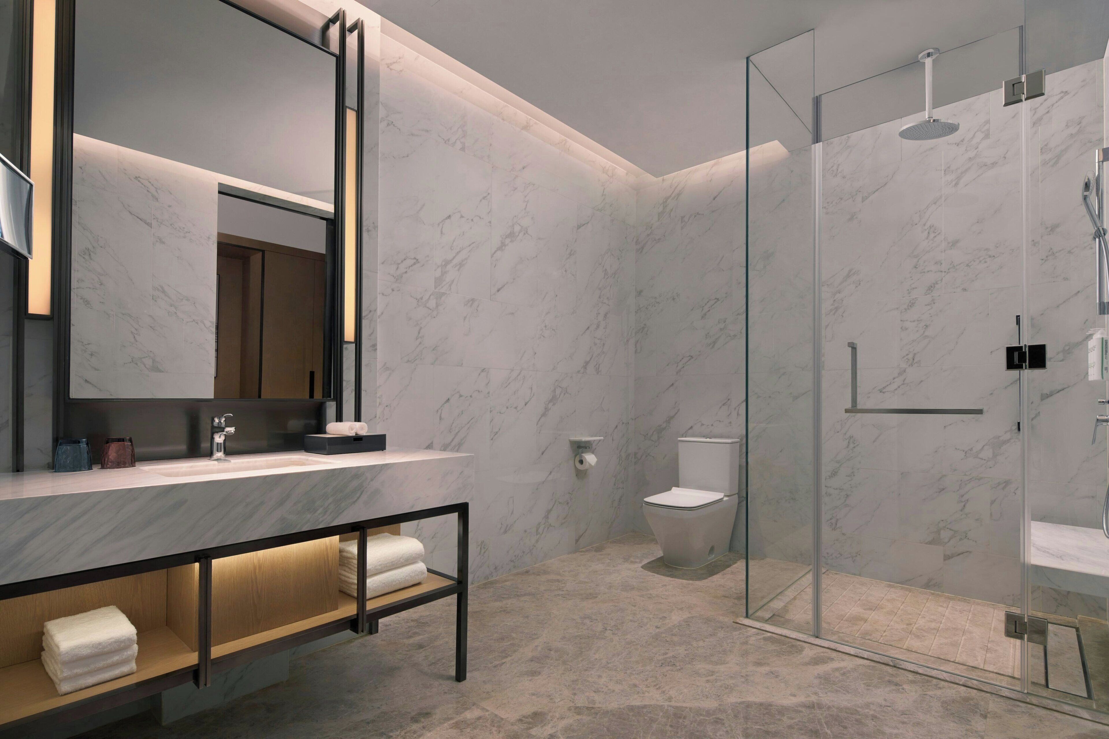 A modern bathroom with a marble vanity, a glass shower enclosure, and a toilet.