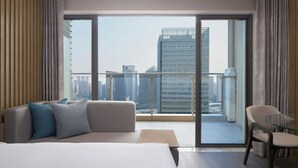 A modern hotel room with a large bed, a sofa, a glass table, and a view of the city skyline through floor-to-ceiling windows. - Courtyard by Marriott Foshan (Foshan)
