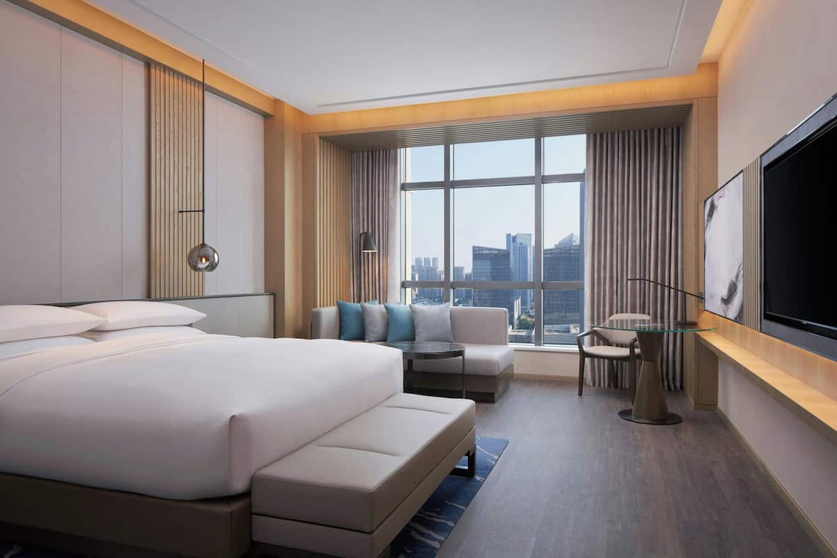 Una habitación de hotel moderna con una cama grande, un sofá, una mesita y un televisor.