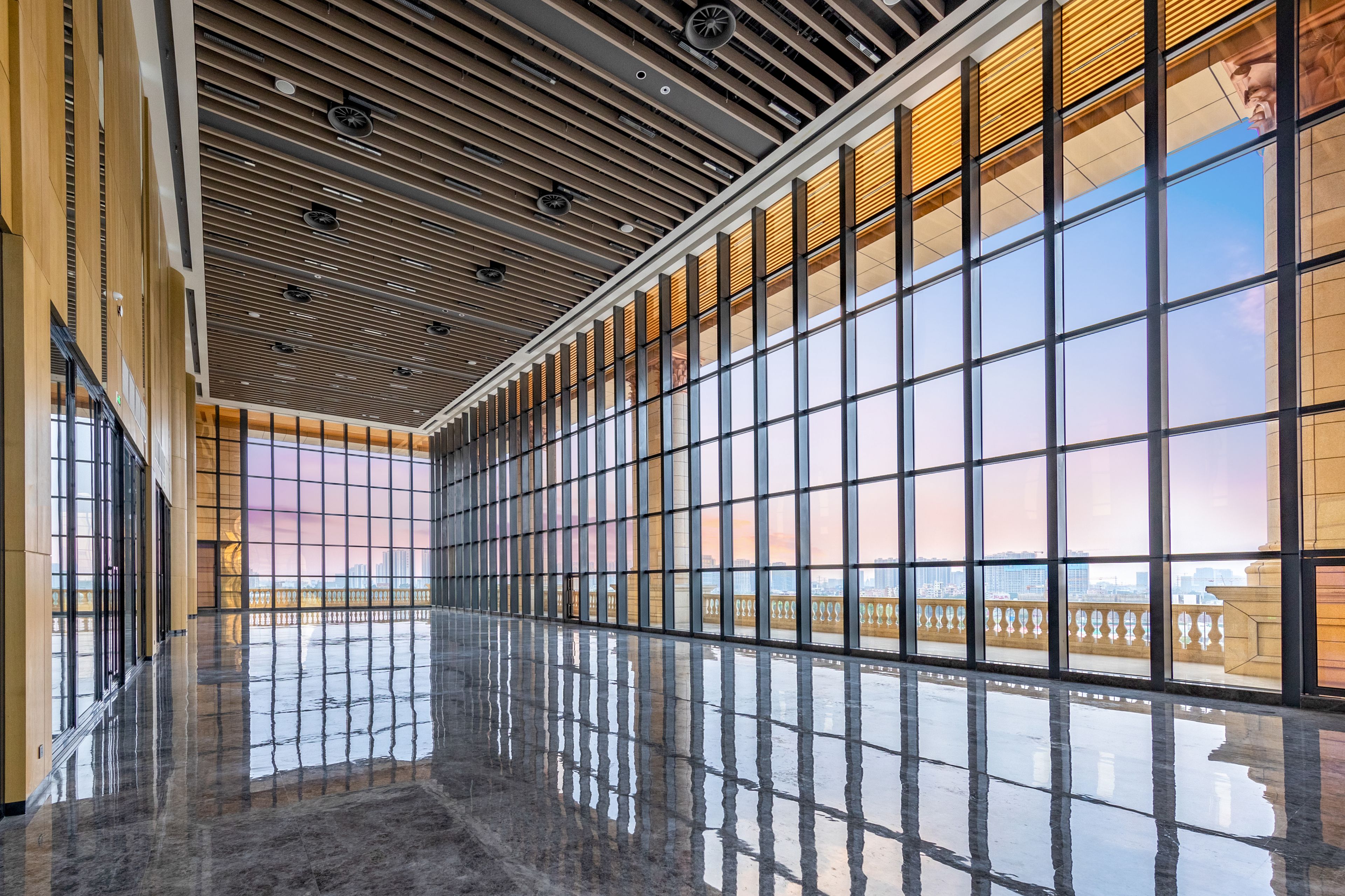 A spacious corridor with reflective floors and large windows offering views of a cityscape.