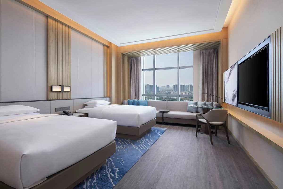 Una habitación de hotel moderna con dos camas, un sofá, un televisor y vistas a la ciudad.