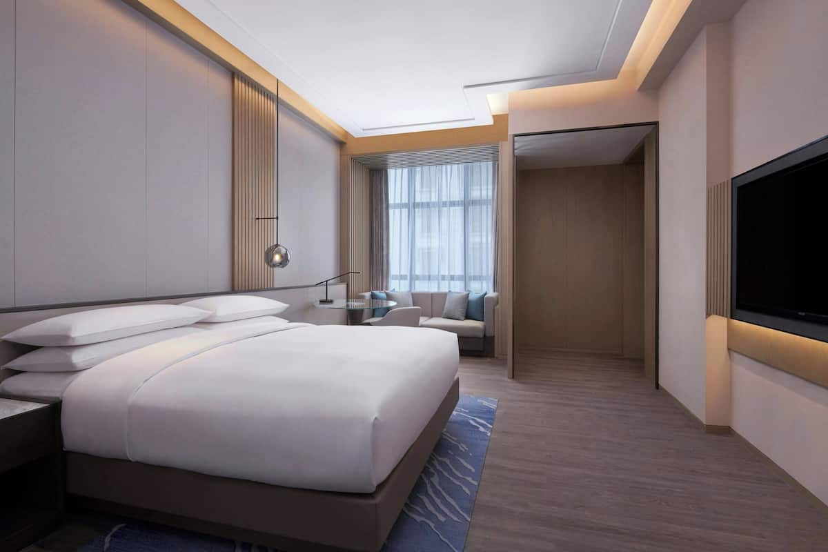 Habitación de hotel moderna con una cama grande, televisión, escritorio y zona de estar con vistas a la ciudad.