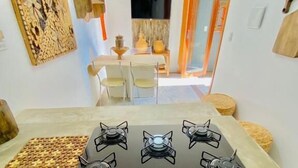 Cozinha moderna com fogão a gás, área de jantar com mesa e cadeiras, e um painel decorativo na parede.