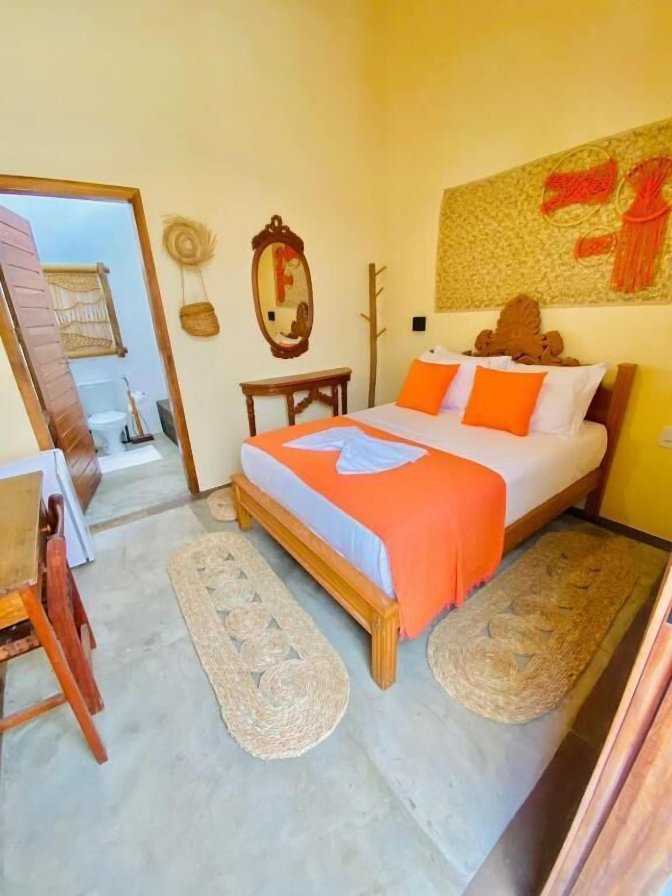 Un dormitorio con cama, dos alfombras, una mesa de madera, un espejo y un adorno en la pared.