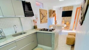 Cozinha moderna com ilha central, forno embutido e pia. É visível uma área de jantar com mesa e cadeiras ao fundo.