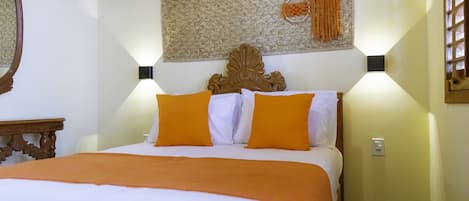 Un lit bien fait, avec une literie blanche et orange, une tête de lit décorative et des appliques murales.
