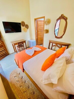 A bedroom with a bed, a wooden nightstand, a chair, a small table, a television, and a mirror. - POUSADA ROOTS - D3 EXPERIENCE (Cruz)