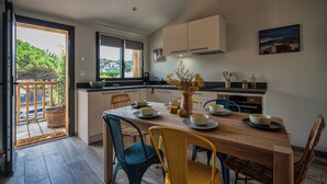 A modern kitchen with a dining area, featuring a wooden table, chairs, and a view of the outdoors. - Magnificent T3 behind the dune (Lacanau)