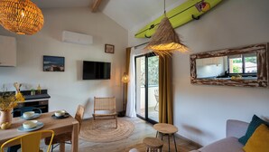 A modern living room with a dining area, a sofa, a TV, and a surfboard decoration. - Magnificent T3 behind the dune (Lacanau)