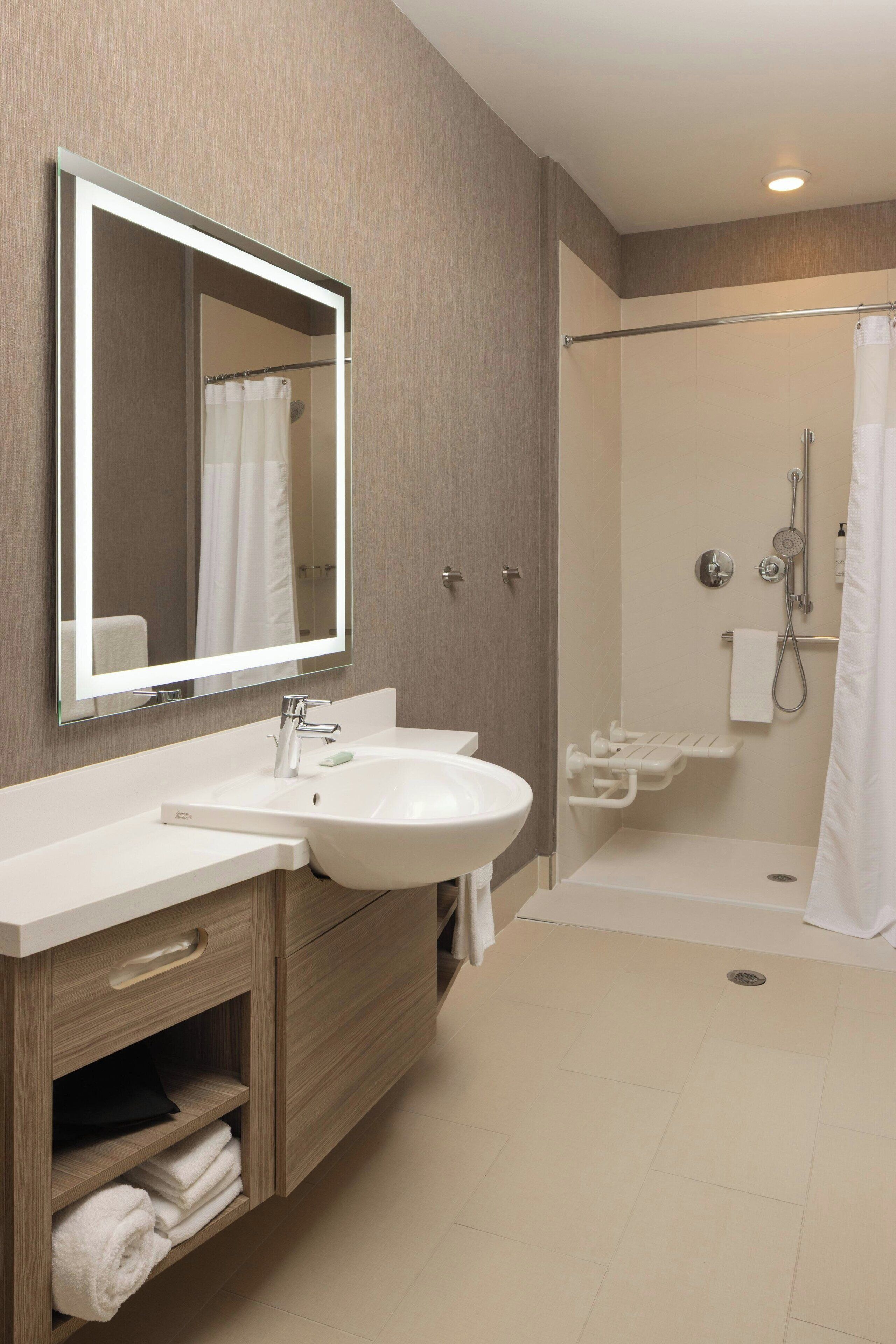 Un baño moderno con un espejo grande, un lavamanos, una ducha y un inodoro.
