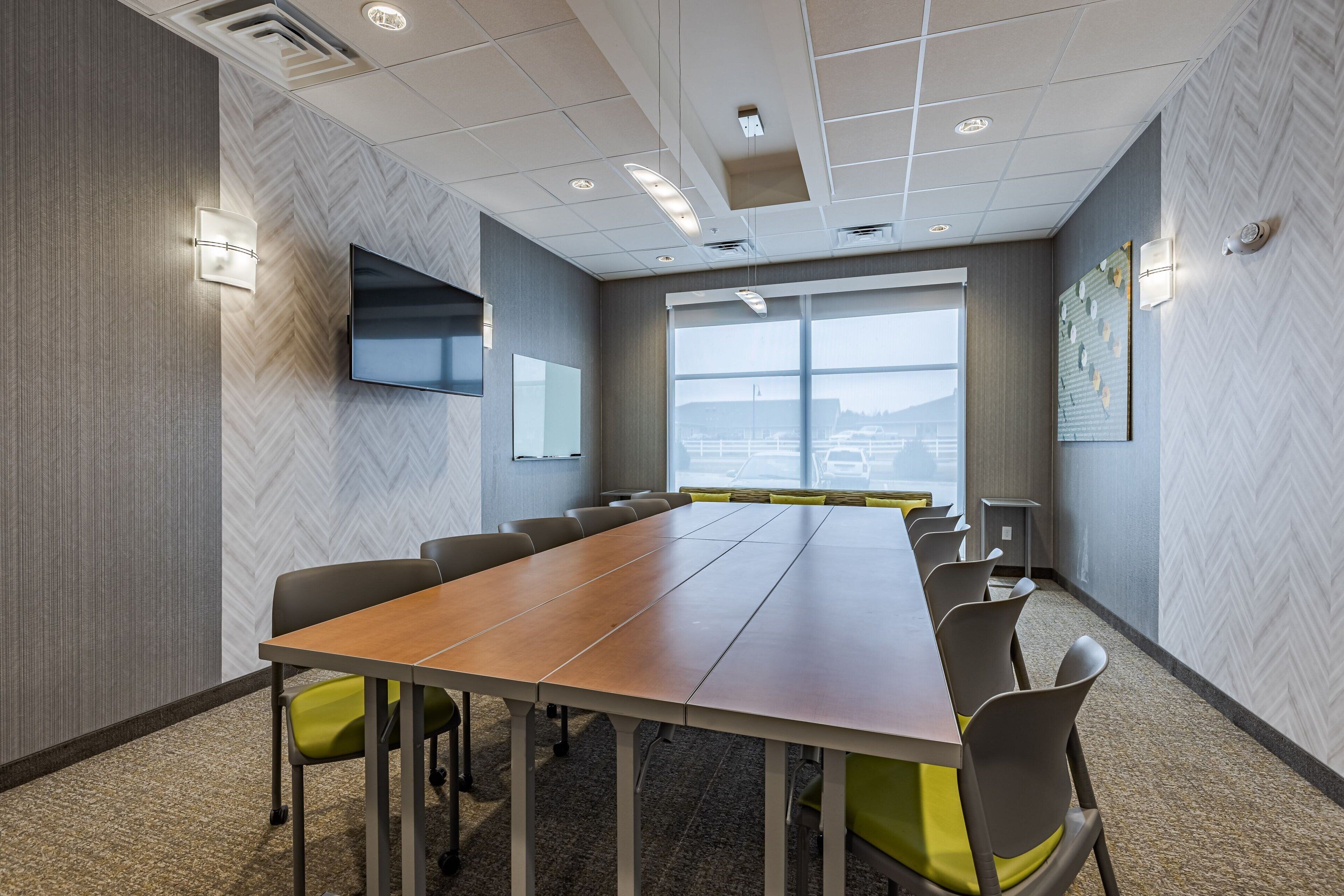 A conference room with a long table, chairs, a flat-screen TV, and large windows with a view.