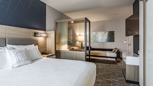 Moderni hotellihuone, jossa on suuri sänky, sohva, työpöytä ja erillinen vaatehuone.