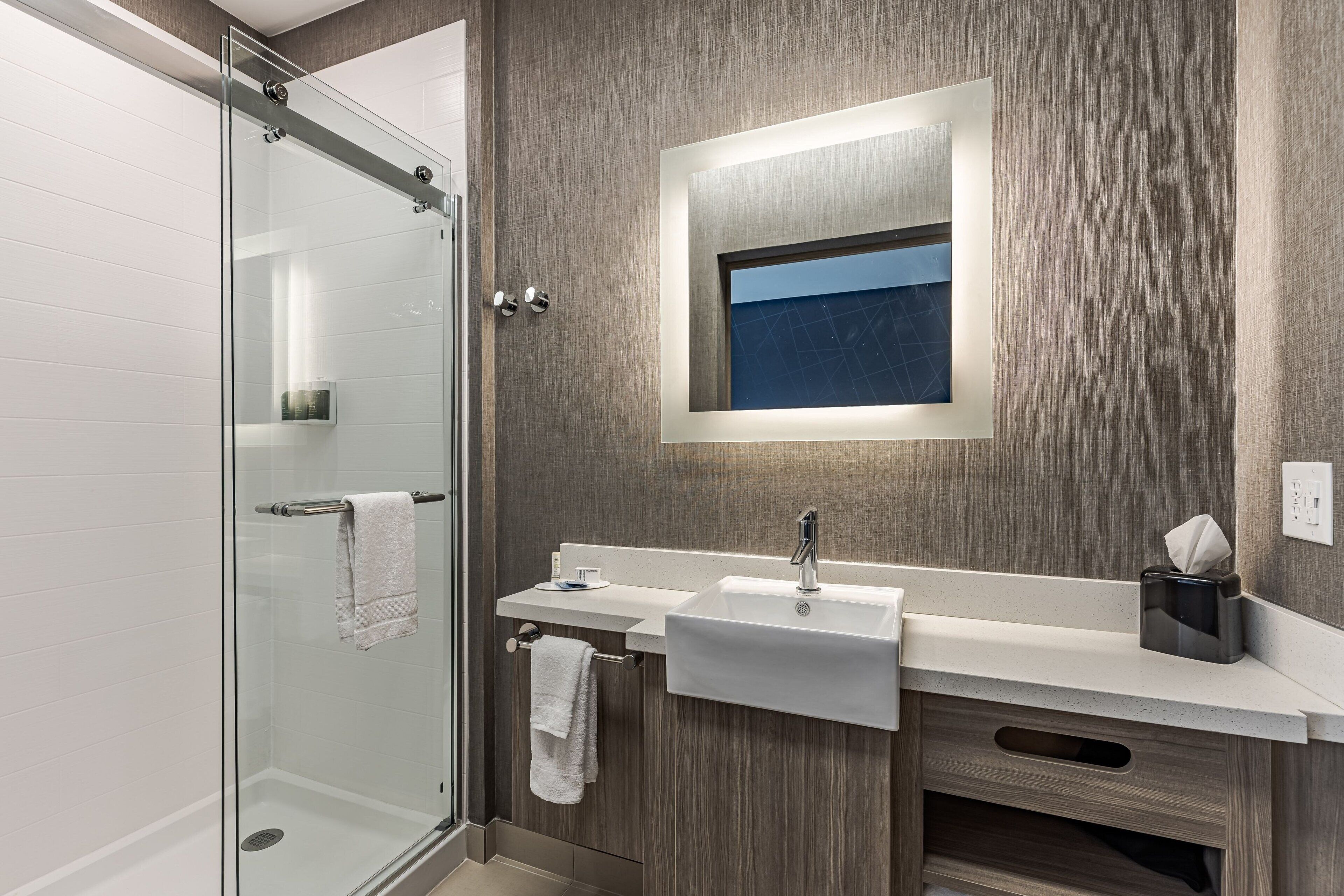 Un baño moderno con cabina de ducha de vidrio, un lavamanos con espejo y un perchero para toallas.