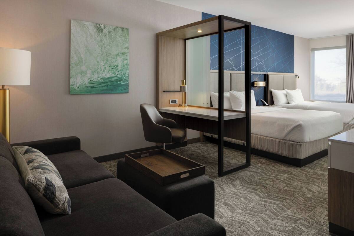 A modern hotel room with a bed, a desk, a chair, and a sofa.