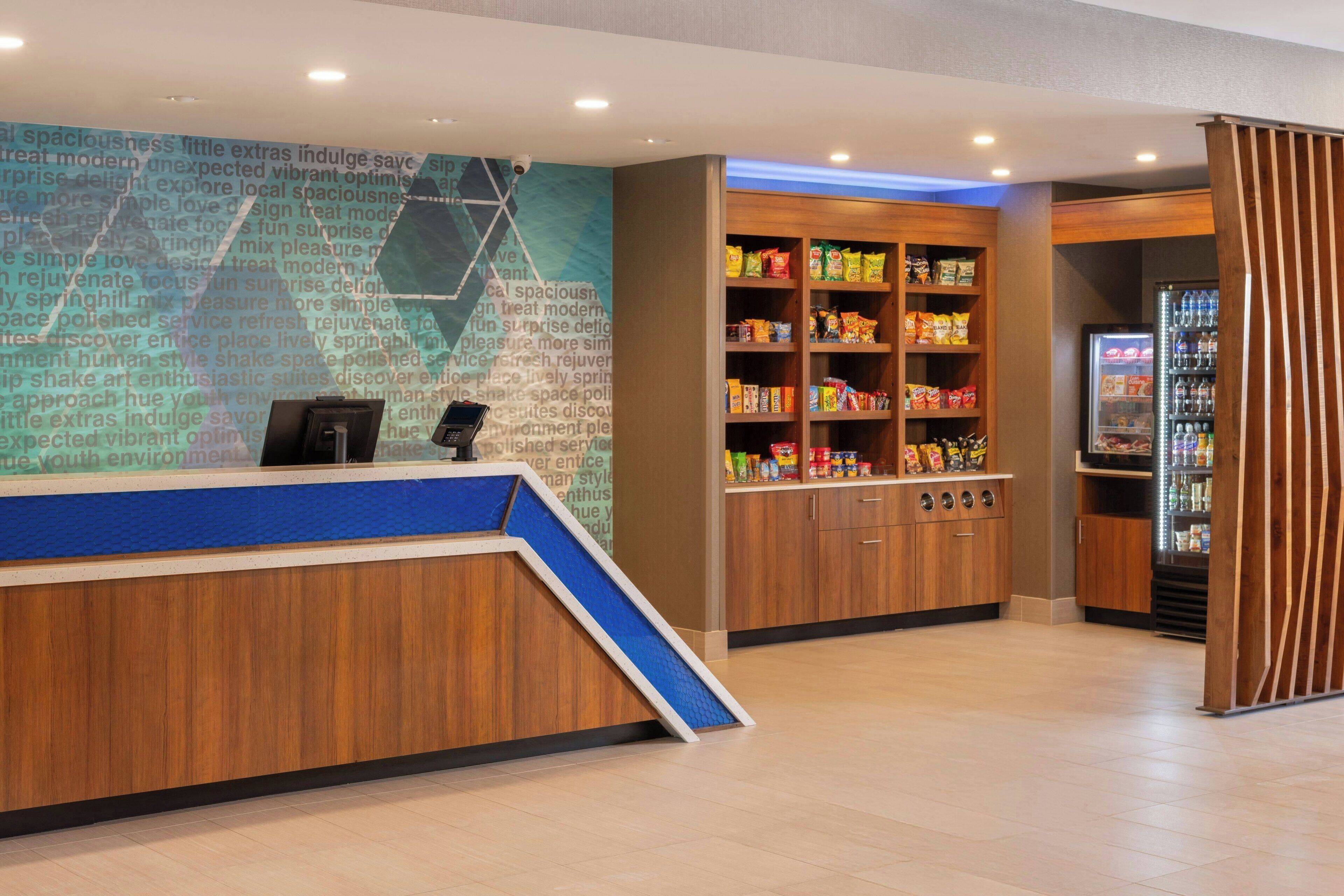 A reception area with a wooden counter, a blue ramp, and a wall with text. There are shelves with snacks and a refrigerator with drinks.