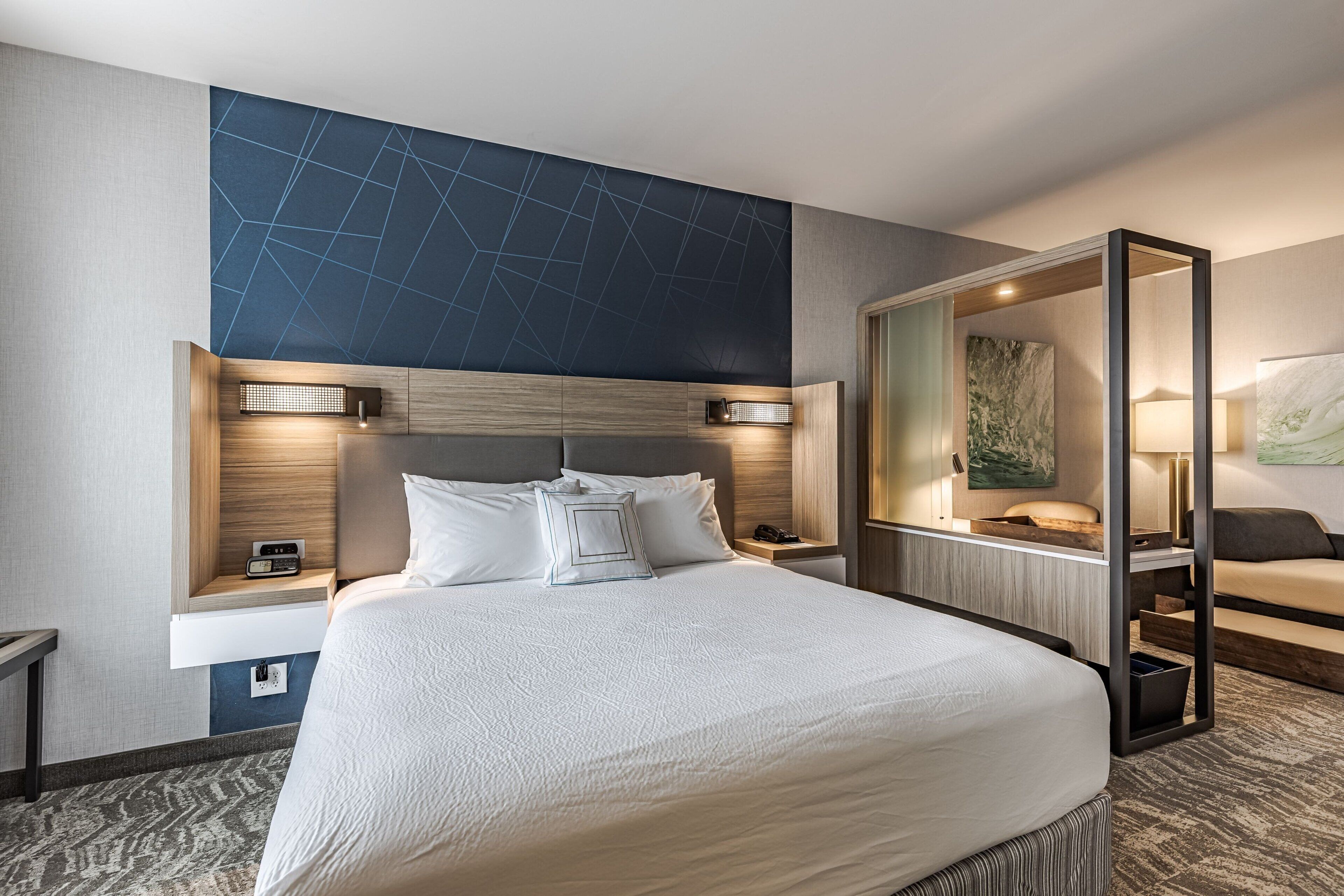 Una habitació d'hotel moderna amb un llit gran, taules de nit, un escriptori integrat i un mirall.